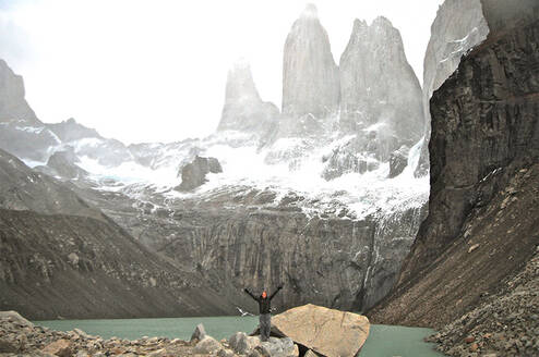 student throwing their arms up while standing on a rock with a vast mountain landscape behind them