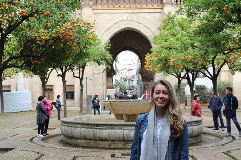 A woman in Spain posing with orange trees in the background.
