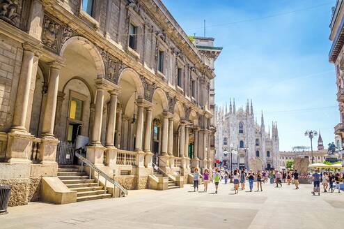 People walk by a tall stone building 
