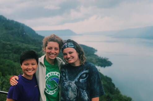 Three volunteers smiling in front of a hill and body of water