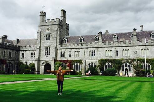 Student with arms stretched out in front of a university building