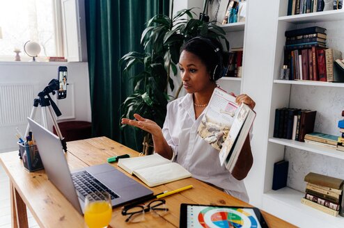 Woman holding up book to computer screen while teaching online.