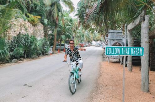 A digital nomad riding his bike past a sign that says "follow your dreams"