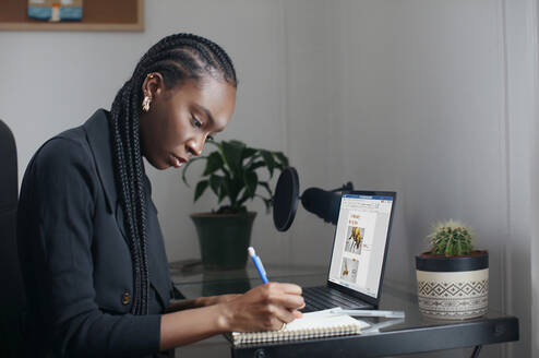 A person sitting in front of a computer while writing in a journal