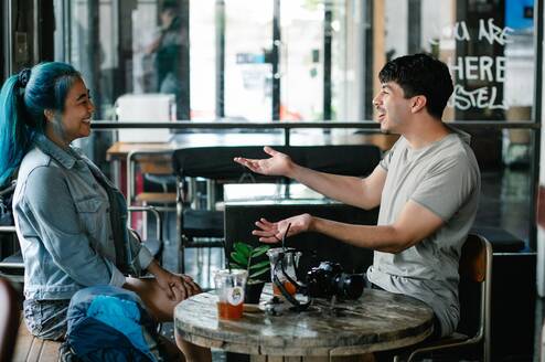 A man and woman sitting at a table talk and laugh.