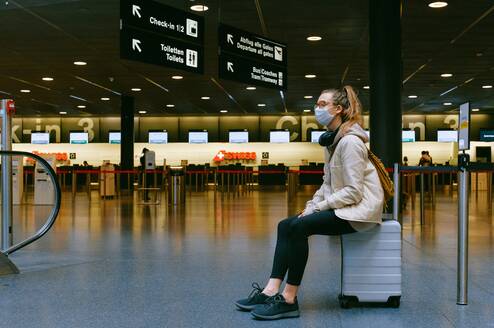Person sitting on suitcase waiting at airport
