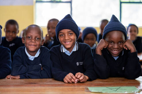 Three smiling boys in school uniforms, sitting together at a desk.