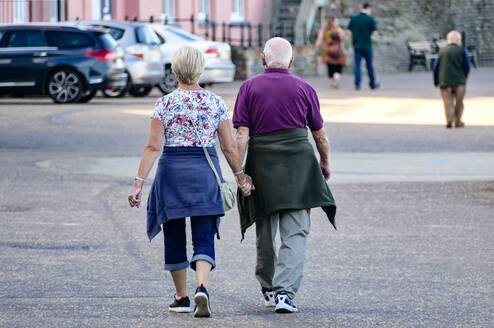 Two older adults holding hands walking down a street