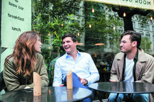 One female and two male postgraduate students sit at a table outside a cafe