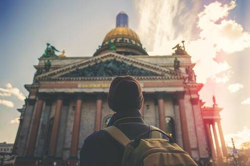 A student with a red beanie and a green backpack facing a building in Germany