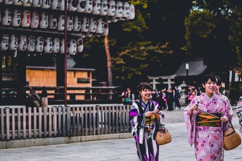 Women dressed in traditional Japanese clothing stand and smile outside.