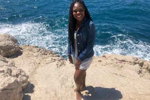 A woman poses smiling in front of an ocean.