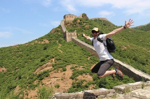 A man jumps in the air smiling on the Great Wall of China.