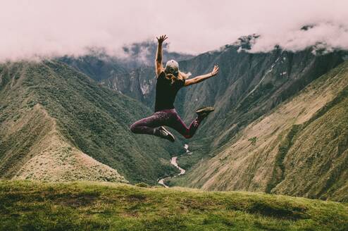 A woman jumps in the air with mountains and valleys in the foreground.