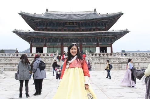 A woman in traditional Korean dress stands in front of a temple.