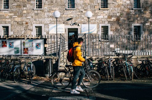A man with a bike stands in front of a university building.