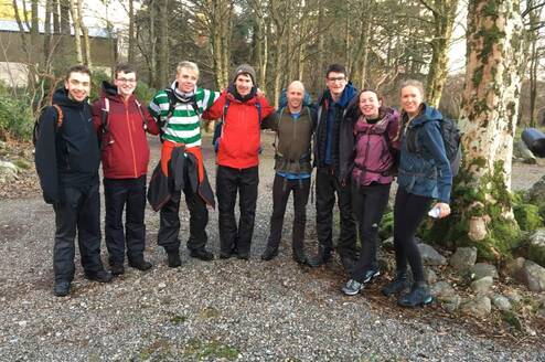 Group of young people in hiking gear. Standing in a line with arms linked, looking happy.