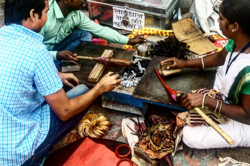 Three people making tools over coals
