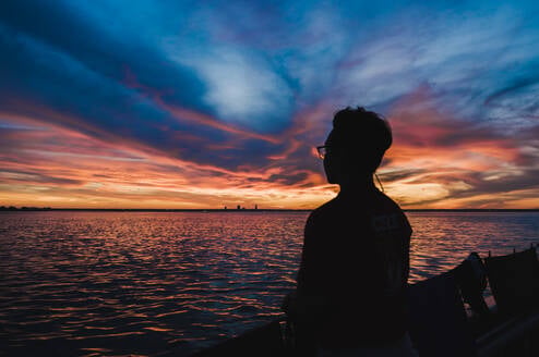 Silhouetted person looking out over the ocean during dusk.