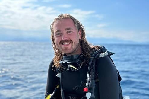 A happy male diver sitting on the edge of the dive boat in full gear smiling at the camera