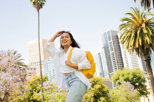 A woman with a backpack pushes her sunglasses up and smiles.