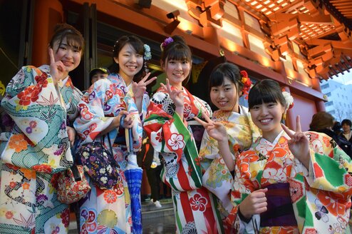 Smiling women in kimonos give the peace sign.