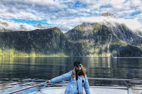 A woman stands on a boat with mountains in the background.