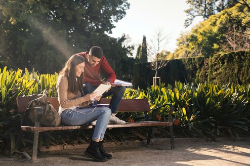 Two students look at a book on a bench.
