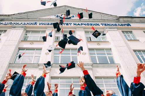 College graduates toss their caps in the air in front of a building.