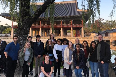 A group of English teachers pose and smile in front of historic Korean architecture.