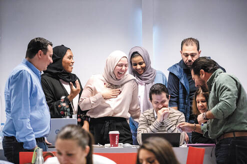 A group of male and female adults crowd around a laptop screen