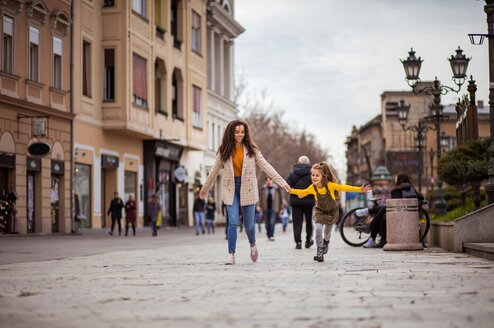 A woman holds hands with a little girl in the street.
