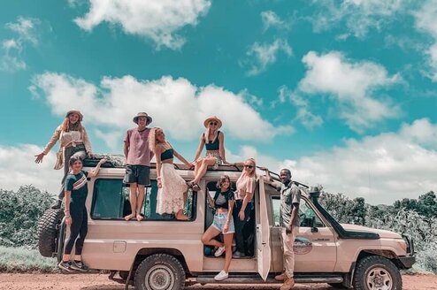 A group of people sit or stand around a safari jeep.