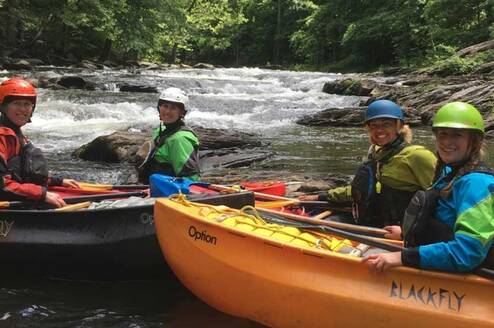 Crew in kayaks on a white water river, on the river bank look over for a picture.