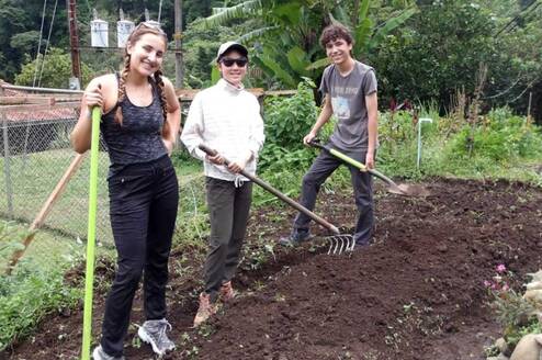 Three students pose for a picture holding gardening tools as they work on a service project.