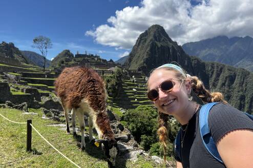 Girl smiling and taking a selfie in front of a llama at Machu Picchu 