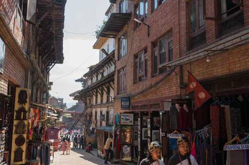 A traditional street scene in Kathmandu with local shops and two people in traditional attire.