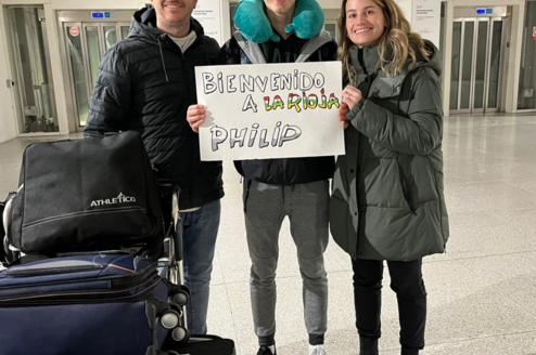 International student arriving in Spain, warmly welcomed by his host family at the airport with a sign saying "Welcome to La Rioja".