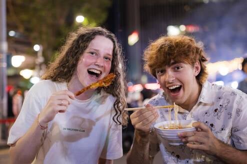EF Gap Year students enjoying Japanese street food in Tokyo at night, laughing together while trying local dishes like ramen and skewers under the city lights.