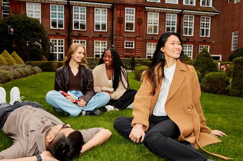 A group of students sitting on a green lawn smiling and talking.