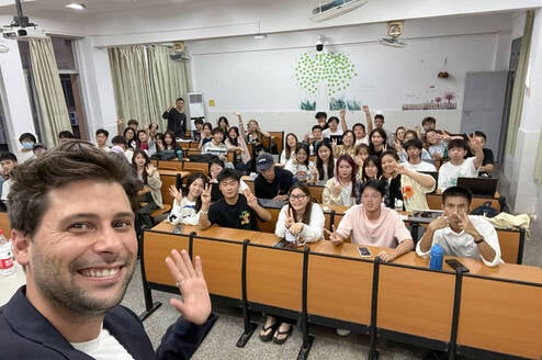 Smiling male TEFL teacher takes a selfie with a classroom full on students.