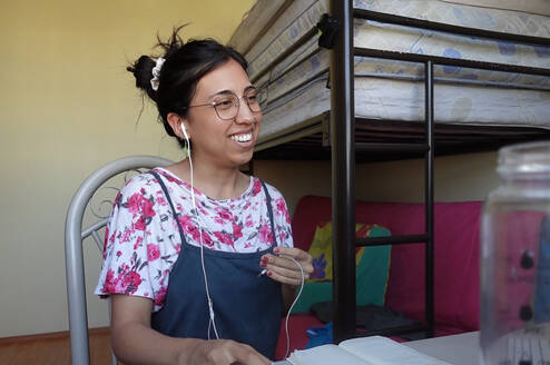 Smiling female TEFL teacher in bedroom teaching English online.