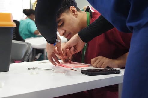 Student practising suturing techniques during a hands-on emergency medicine summer school in Liverpool