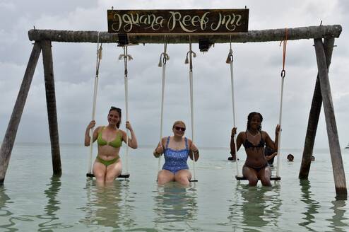 Three teen travelers sitting on a swing in the ocean in Belize