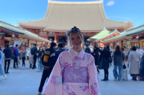 Smiling intern in kimono standing in front of a temple
