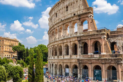 Sunlit view of the ancient Colosseum in Rome with visitors exploring the entrance.