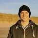 Niall Coombes wearing a black beanie and black zip up jacket smiling 