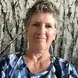 Jackie Bertrand Dix Jackson with short grey hair, earrings, and a blue geometric shirt smiling at the camera