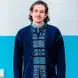 William Davies wearing a blue traditional shirt and navy cardigan with long brown hair and blue eyes
