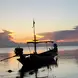 A boat on the ocean with the sun setting behind it
